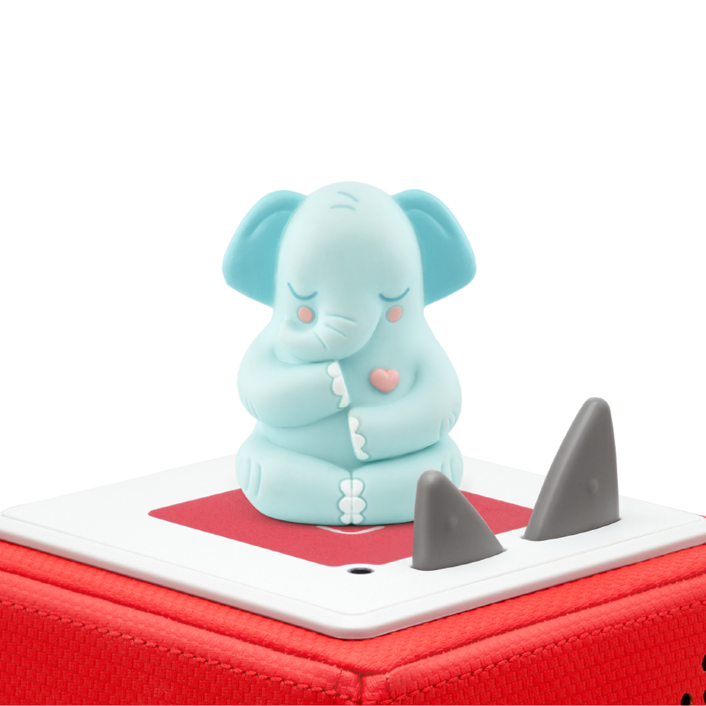 Cute blue elephant figurine with a pink heart sits on a red and white box against a white background. The scene conveys calmness and playfulness.