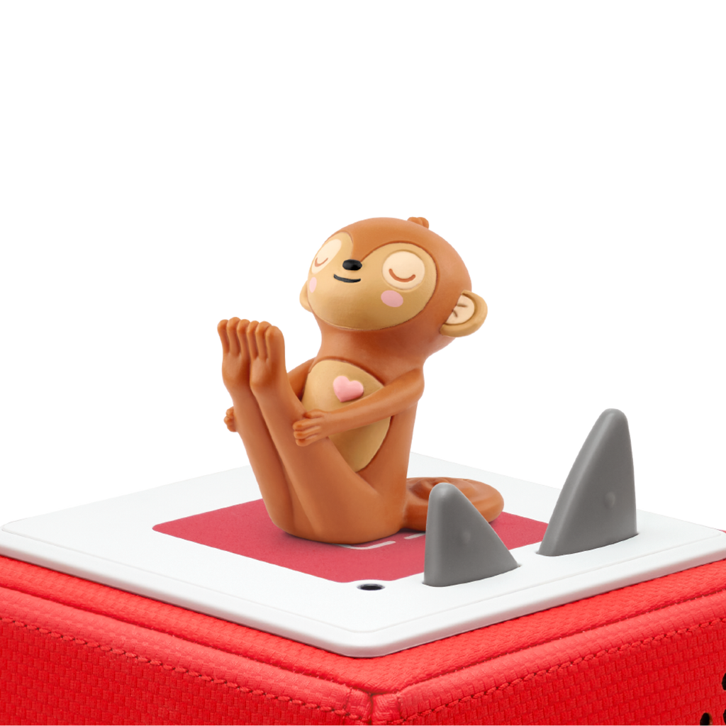 A cute, smiling monkey figurine with closed eyes sits on a red and white base. It has a heart on its chest, conveying a peaceful, joyful vibe.