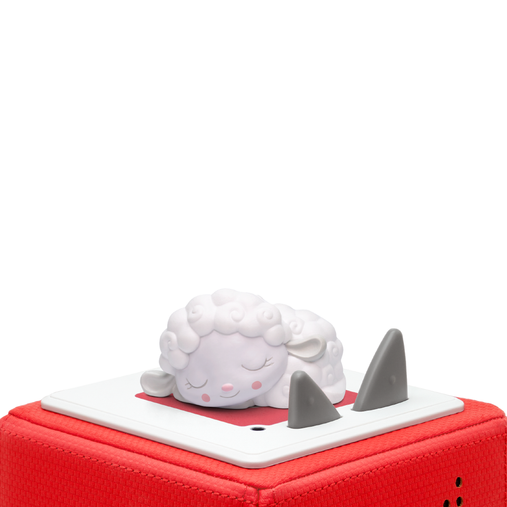 A cute figurine of a sleeping white sheep with closed eyes lies atop a red box. The box has a square white platform and two gray triangular shapes.