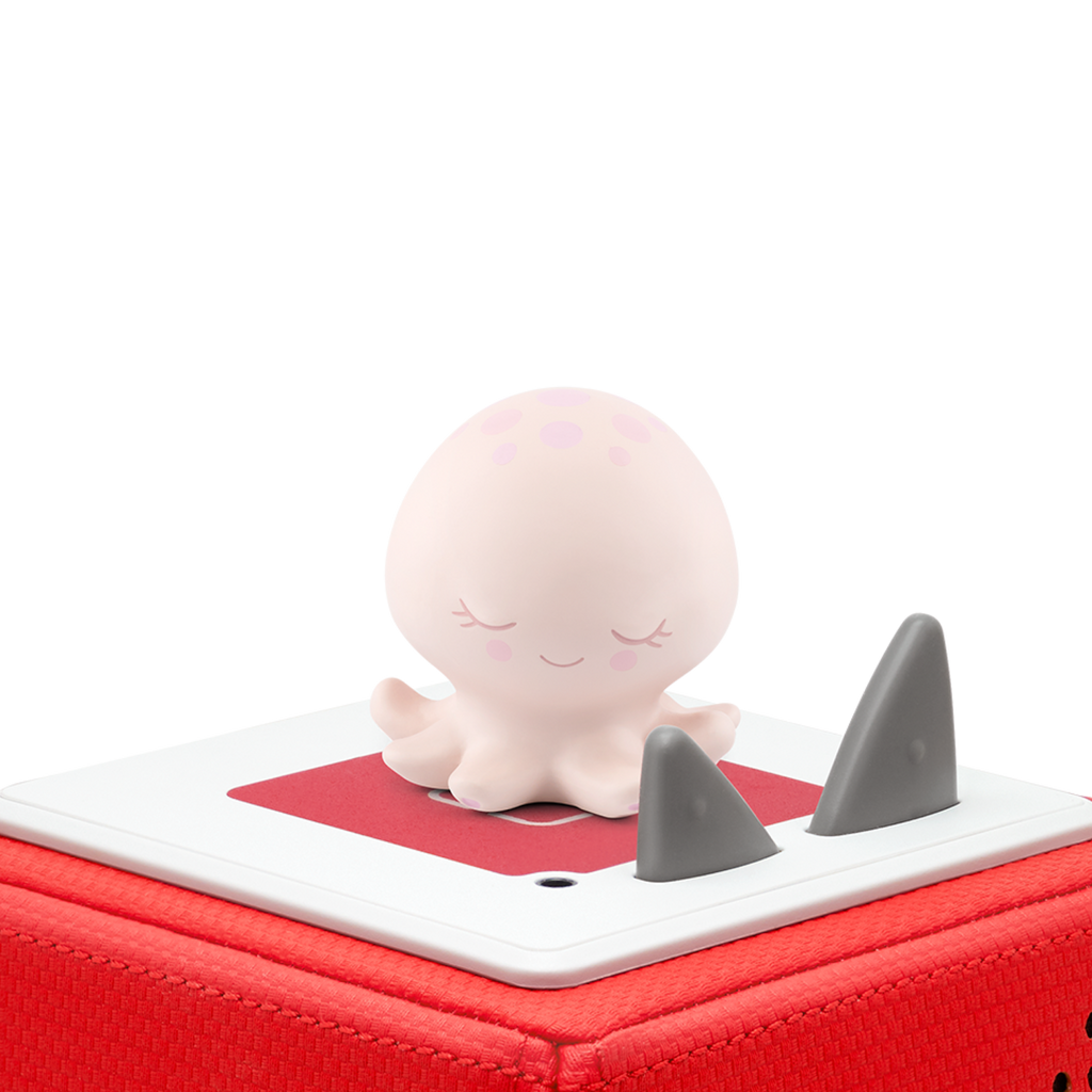 Cute smiling octopus figurine on a red speaker box with gray fins, against a solid white background. The mood is playful and cheerful.