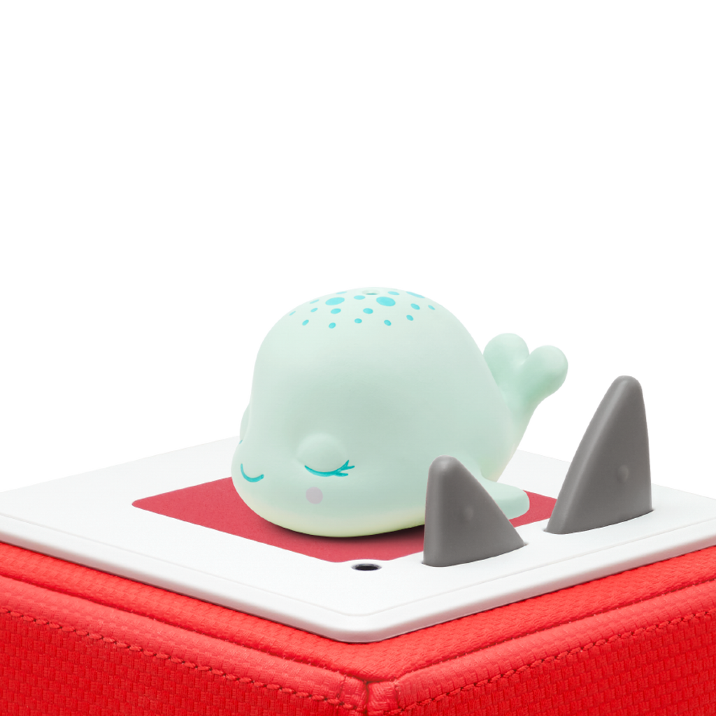 A cute, mint-green whale figurine rests serenely on a red square base with its eyes closed, surrounded by grey triangular points, set against a white background.