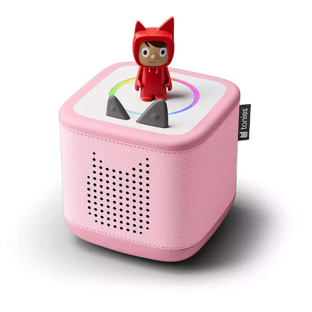 Pink Toniebox speaker with a cute figure in a red outfit on top. The box has ear-like gray knobs, a perforated design, and a playful appearance.