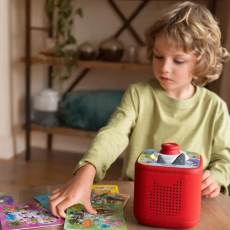 A child plays a game using game cards and a red Toniebox with a Monster Talent Search topper.