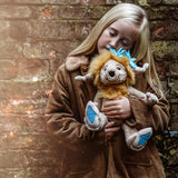A young blonde girl in a jacket lovingly hugs a plush creature against a rustic brick background.