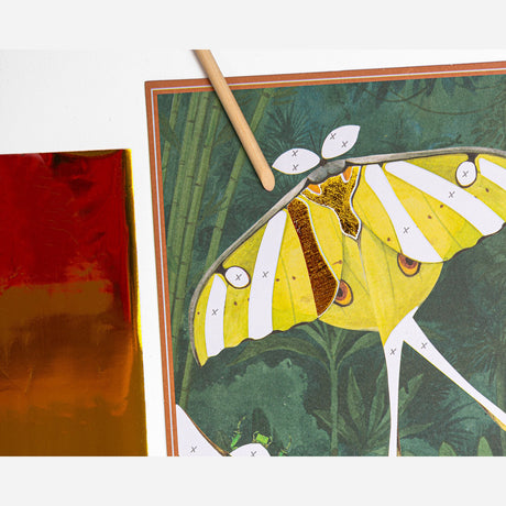 Applying gold foil to a Tout Autour du Monde moth activity board using a wooden stylus and transfer sheet.