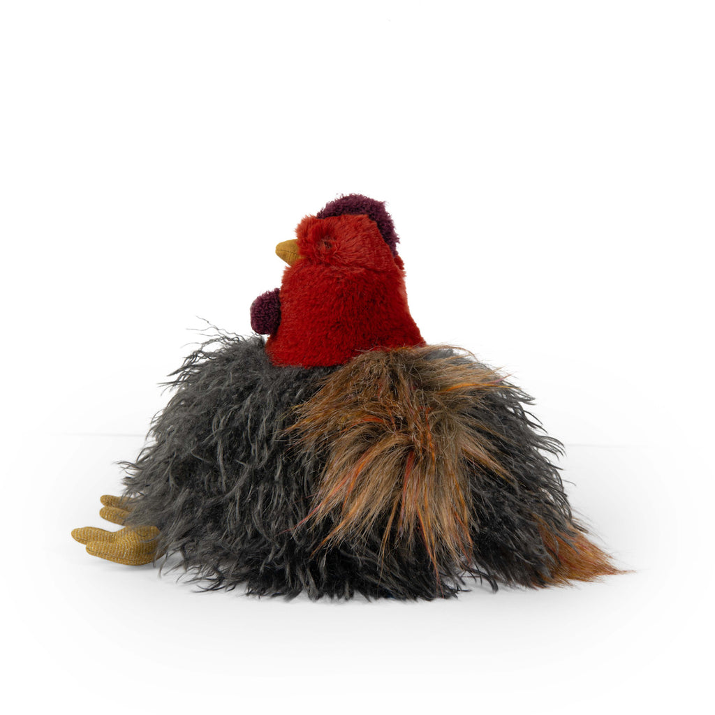 Fluffy plush chicken toy with a red head and yellow beak, featuring long, shaggy, black and brown body fur, sitting on a white background.