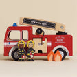 Wooden red toy fire engine with ladder, two firefighter figurines, and two small wooden fire cutouts.