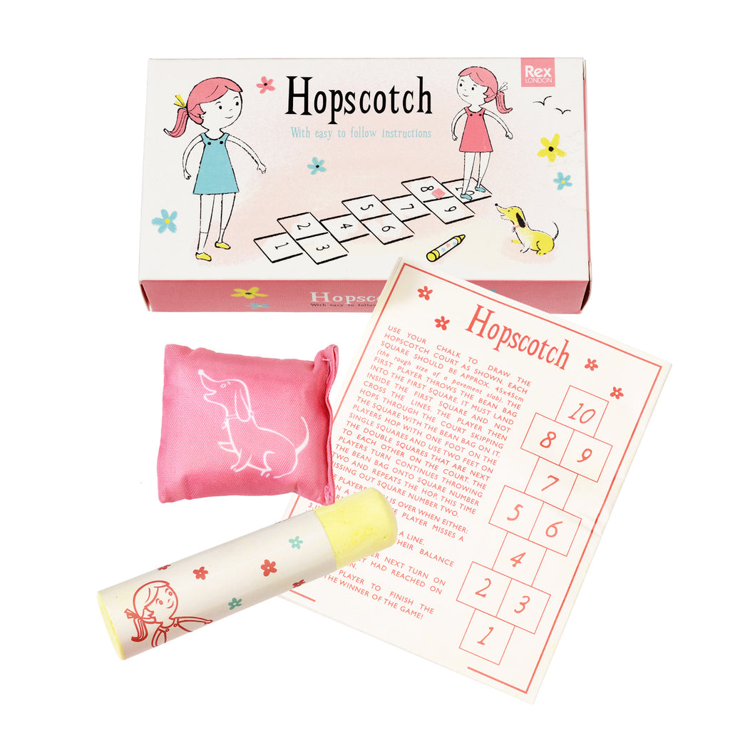 Hopscotch game set with instructions, pink beanbag featuring a white dog silhouette, yellow chalk wrapped in illustrated paper, and pastel box.