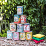 Stacked vintage-style game tin cans on a wooden log outdoors with three bean bags beside them.