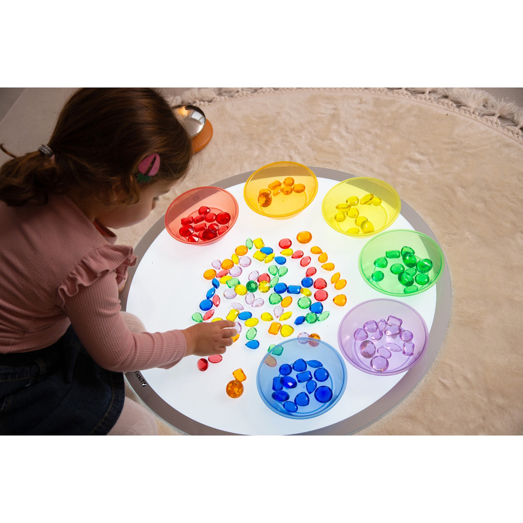 A collection of brightly colored, see-through plastic gems, ideal for sensory play, sorting, counting, and light table activities.