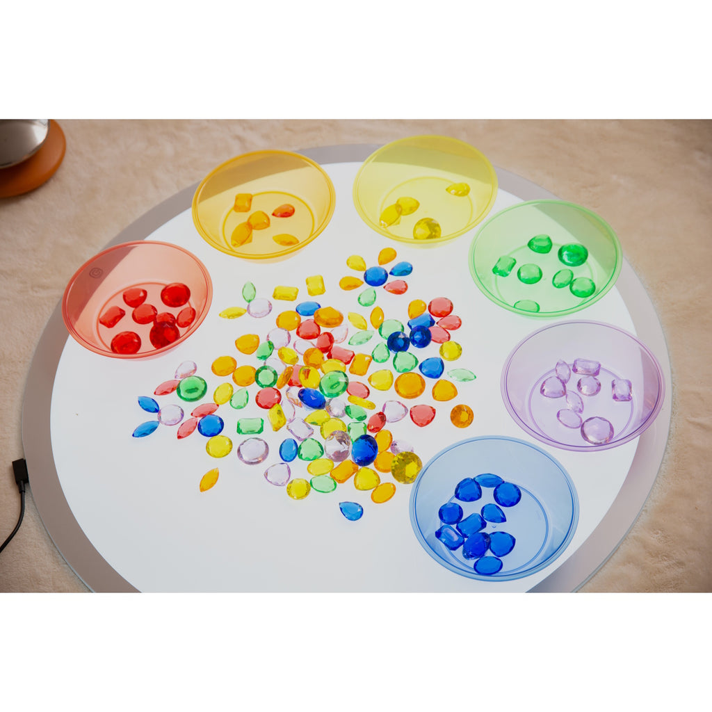 A collection of brightly colored, see-through plastic gems, ideal for sensory play, sorting, counting, and light table activities.
