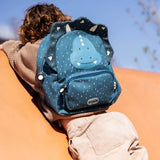 A child climbing a structure while wearing a blue triceratops dinosaur backpack with white speckles.