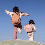 Two children seen from behind wearing pink animal backpacks, a cat and a butterfly, against a clear blue sky.