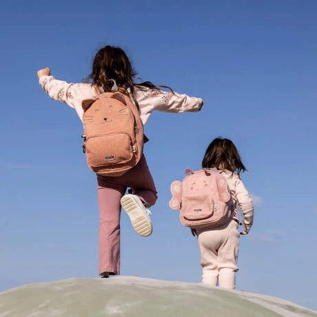 Two children seen from behind wearing pink animal backpacks, a cat and a butterfly, against a clear blue sky.