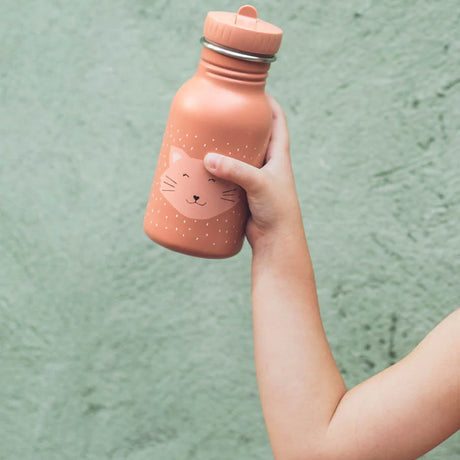 A child's hand holding up a peach-colored cat water bottle against a textured green background.