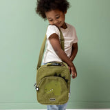 Young child carrying a green dinosaur-themed lunch bag over their shoulder against a solid green background.