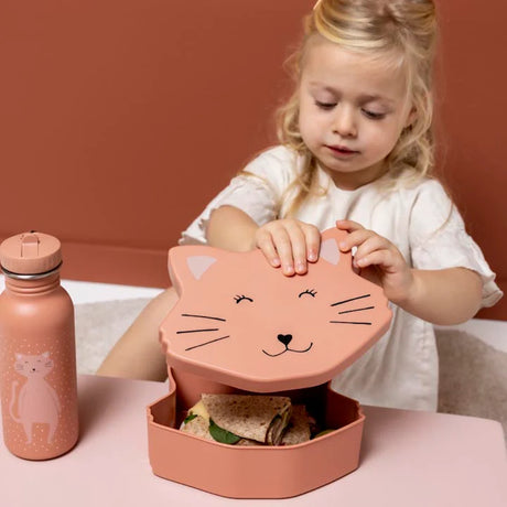 A young girl opens a pink cat-shaped lunch box containing a sandwich, next to a matching cat water bottle.
