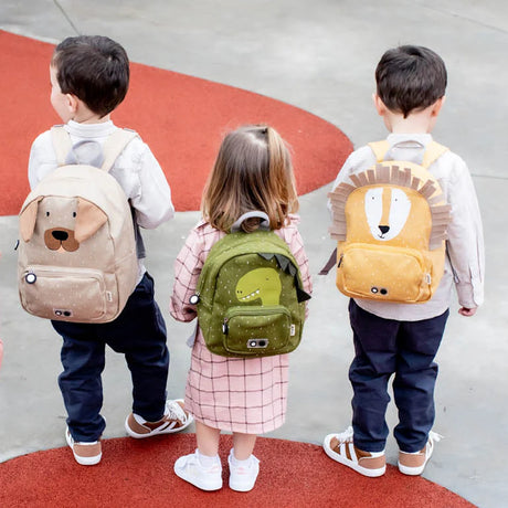 Three young children standing from behind, wearing a dog, dinosaur, and lion animal backpack.