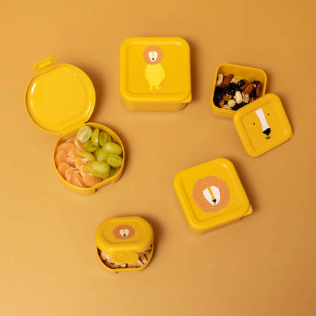 An assortment of yellow lion-themed snack containers, some open with fruit and nuts, on a yellow background.