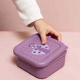 A child's hand opening a purple nesting snack box with a cartoon peacock illustration on the lid.