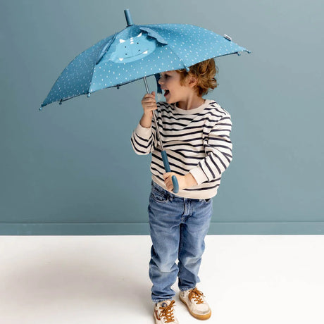 A smiling toddler in a striped sweater holds a blue, patterned dinosaur umbrella with pop-out ears.