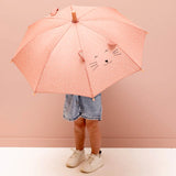 A child holding a pink umbrella with a cartoon cat face, fabric ears, and white specks.