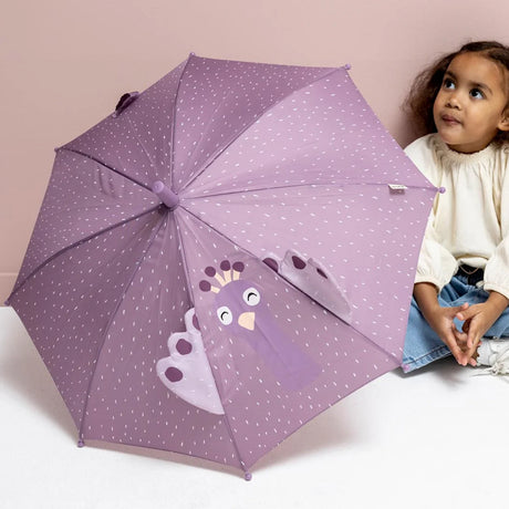 A child sitting next to a purple umbrella decorated with white dots and a cartoon peacock character.