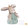 Plush rabbit toy wearing a pointed hat and floral overalls, standing next to a small white music box.
