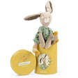 Stuffed rabbit toy wearing a green dress, sitting on a yellow cylindrical gift box with an illustrated bunny on it.