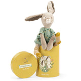 Stuffed rabbit toy wearing a green dress, sitting on a yellow cylindrical gift box with an illustrated bunny on it.