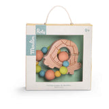 A Moulin Roty wooden turtle teething rattle in its packaging, featuring colorful beads on a circular ring.