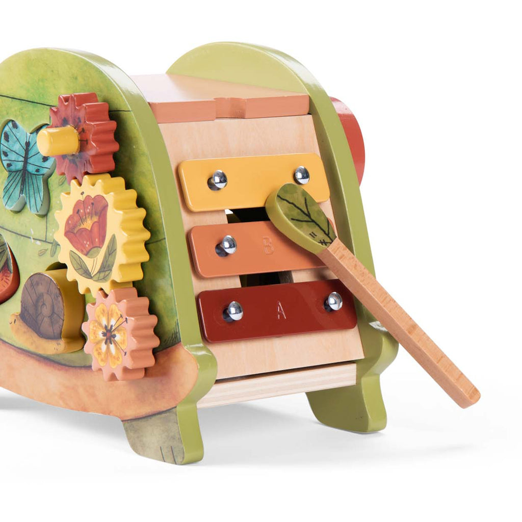 Colorful wooden activity toy featuring a xylophone with a leafy mallet, spinning gears, and nature-themed designs. Playful and educational tone.
