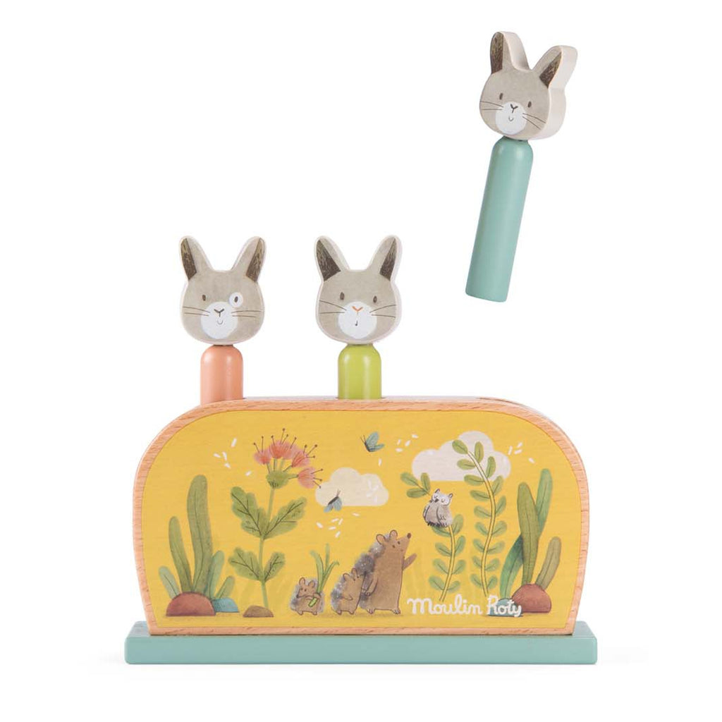 Toy with three pop-up rabbit heads in pastel colors on green and yellow base. Base decorated with plants and animals, creating a playful scene.