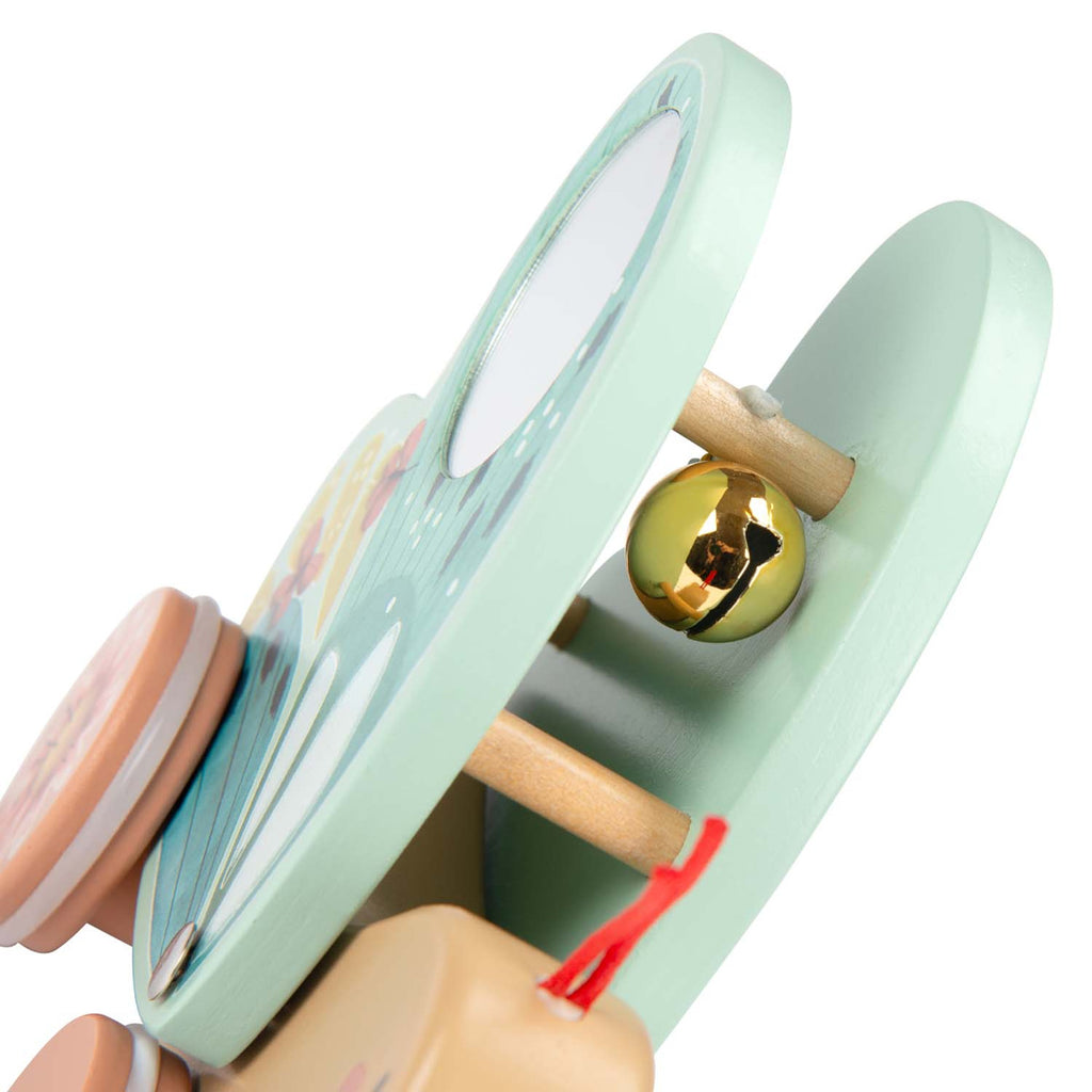 Close-up of a pastel green wooden toy with a reflective mirror, gold bell, and red string. The playful design conveys a cheerful, whimsical tone.
