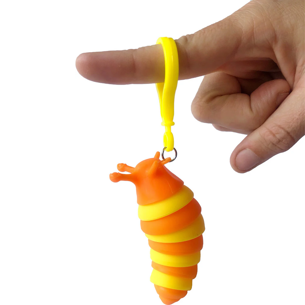 A hand holding a small, orange and yellow, worm-shaped toy keychain by a yellow loop. The toy's expression is playful and cheerful.