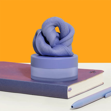 Periwinkle focus putty on its container, placed on a purple notebook with a matching pen.