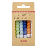 A set of colorful twisted cake candles in blue, green, yellow, orange, and white are visible through a cardboard box with "12 Twisted Cake Candles" text.