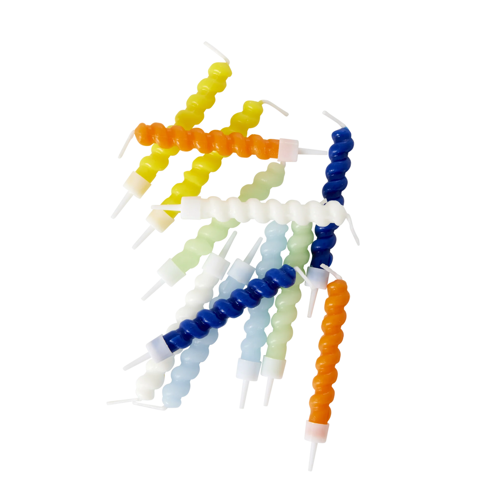 Brightly colored spiral candles in hues of blue, orange, yellow, and white are scattered on a white background, creating a playful and vibrant look.