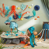 Children in ocean costumes playing near a decorated party table under an Under the Sea themed garland.