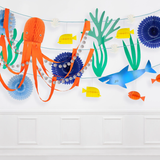 Under the sea garland with paper cutouts of an orange octopus, blue shark, and sea life hanging on a white wall.