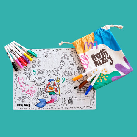 An ocean-themed coloring mat with markers and a colorful "Born Bizzy" drawstring bag on a teal background.