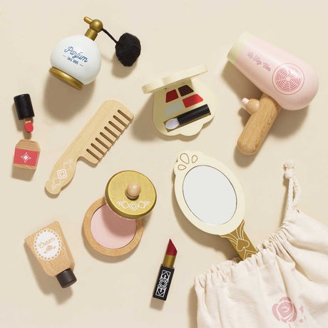 Flat lay of wooden toy cosmetics, hairdryer, mirror, comb, and perfume next to a cloth drawstring bag.