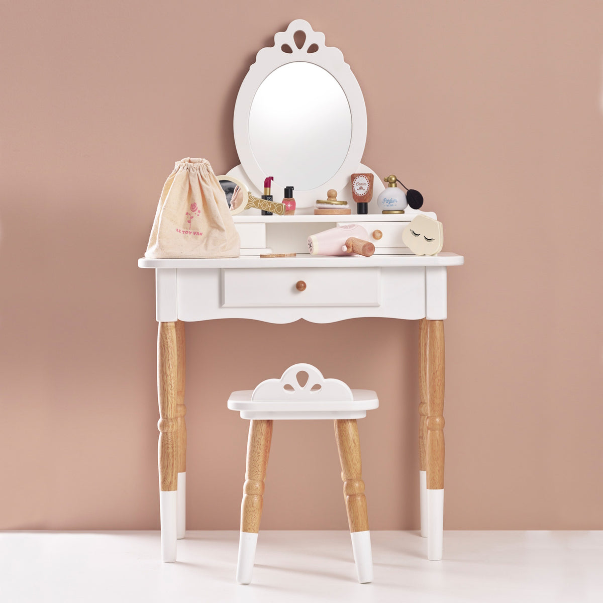 White wooden toy vanity table and stool set up with play beauty accessories and a storage bag.