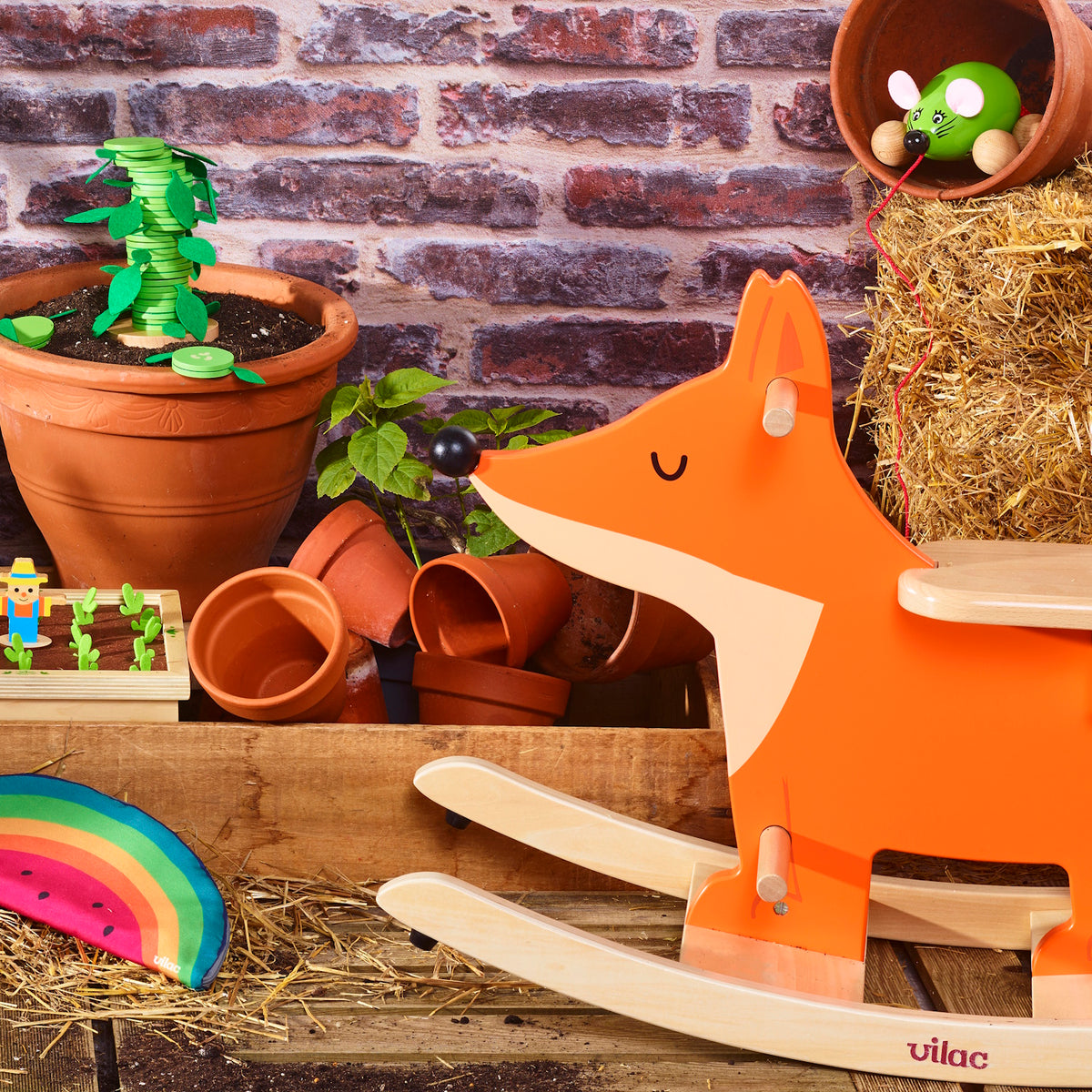 Vilac wooden fox rocker in a garden setting with terracotta pots, hay, and a green toy mouse.
