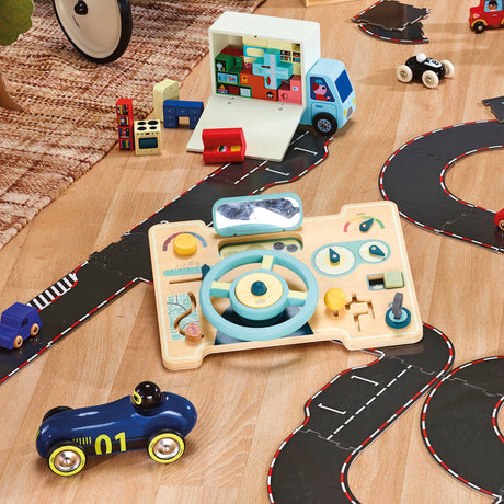 Wooden toy dashboard, toy cars, and delivery truck set on a black play road track over a light wood floor.