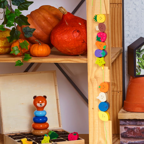 Vilac wooden lacing beads hanging on a shelf with pumpkins and a toy bear stacker in a cozy room.