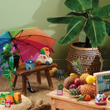 Wooden toy lion car on a rustic stool with a rainbow umbrella, tropical plants, fruits, and blocks.