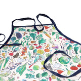 Kitchen apron with a colorful vegetable and herb print, featuring dark blue straps and a matching front pocket.