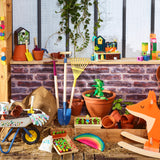 Colorful wooden garden toys including a wheelbarrow, rake, shovel, and fox rocker displayed against a brick wall.