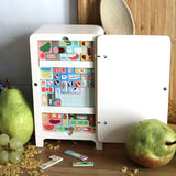 Wooden toy fridge puzzle with colorful Tetris-like food blocks, next to real pears and grapes.